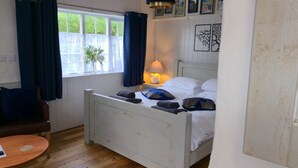 A bedroom with a bed, a chair, a small table, a window with curtains, and wall decorations. - The George & Dragon Pub - The Stable (Horsham)