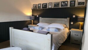 A bedroom with a bed, two bedside tables, a chair, and wall-mounted picture frames. - The George & Dragon Pub - The Hayloft (Horsham)