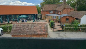 A traditional brick building with a red roof, a covered patio area with tables and umbrellas, and a car parked in the foreground. - The George & Dragon Pub - The Hayloft (Horsham)