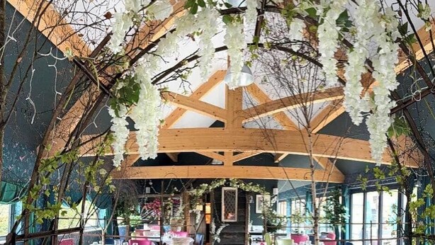 A pub interior with tables and chairs, a wooden ceiling structure, and hanging white flowers. - The George & Dragon Pub - The Hayloft (Horsham)