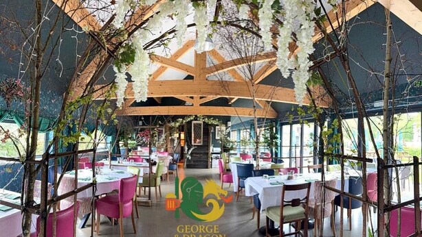 A pub interior with tables and chairs, a wooden ceiling structure, and hanging white flowers. - The George & Dragon Pub - The Apartment (Horsham)