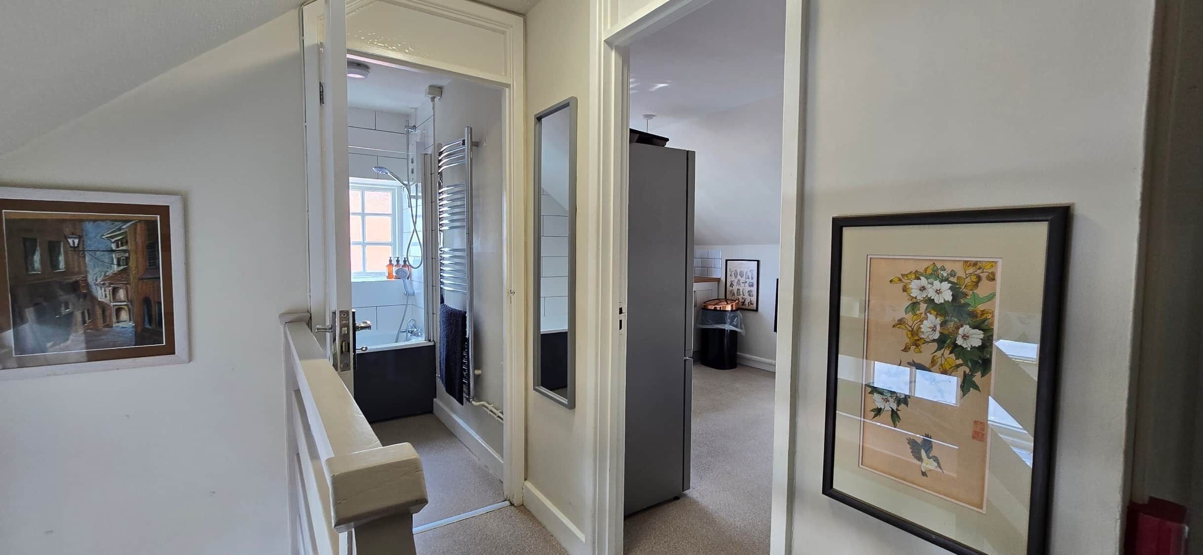 A hallway with a shower, a door leading to a room, and framed artwork on the walls.