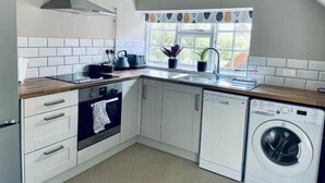 A modern kitchen with white cabinets, a built-in oven, a dishwasher, and a window with a view of greenery. - The George & Dragon Pub - The Apartment (Horsham)