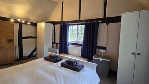 A bedroom with a large bed, a wardrobe, a radiator, and a window with curtains. - The George & Dragon Pub - The Apartment (Horsham)