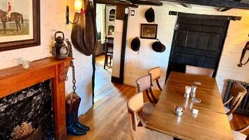 A wooden dining table with chairs, a fireplace with a mantle, and a wall with mounted hats and a framed picture.