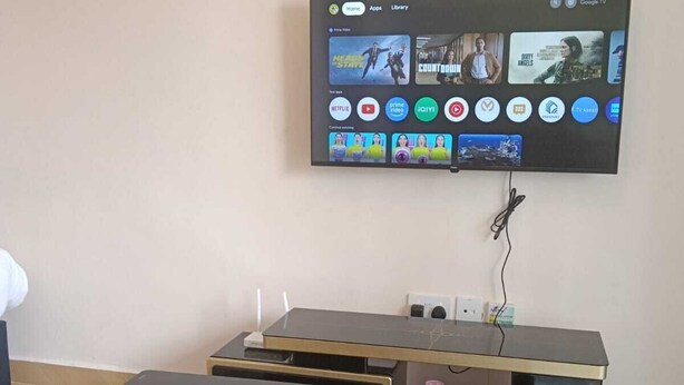 A living room with a flat-screen TV mounted on the wall displaying various streaming apps. There are two black coffee tables with gold accents and a small drawer.