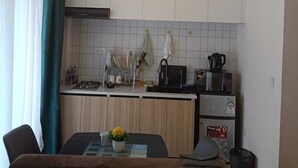 A compact kitchen with white cabinets, a dining table with chairs, a hanging light fixture, and a microwave.