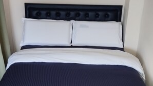 A bed with a dark blue mattress and white pillows, a headboard with a tufted design, and a light-colored rug on the floor.