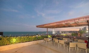 Eine Terrass mit Tischen und Stühlen mit Blick auf eine Stadtlandschaft und das Meer.