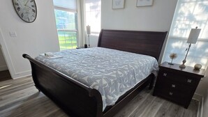 Un dormitorio con cama, mesita de noche, reloj de pared y ventana.