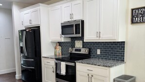Una cocina moderna con armarios blancos, un refrigerador negro, microondas, horno y un cubo de basura de acero inoxidable.