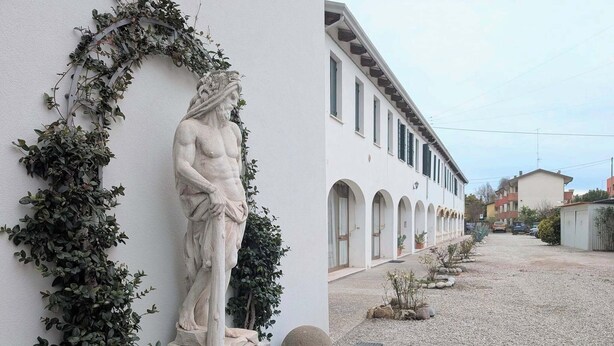 A white building with a statue of a man on a pedestal, surrounded by greenery. - Rialto Apartment (Dolo)