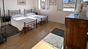 A bedroom with two beds, a wooden dresser, a nightstand, a ceiling fan, and a window with a view of buildings. - Rialto Apartment (Dolo)