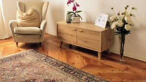 A room with a beige armchair, a wooden cabinet, a flat-screen TV mounted on the wall, a floral vase, and a patterned rug on the wooden floor. - Rialto Apartment (Dolo)