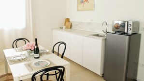 A compact kitchen with white cabinets, a stainless steel refrigerator, and a dining area with a white table set for two. - Rialto Apartment (Dolo)
