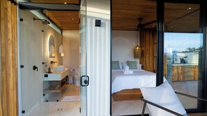 A modern hotel room with a glass door leading to a balcony, a bed with white linens, a small sitting area, and a view of the outdoors. - Casita Kai by Wynwood House (Cobano)