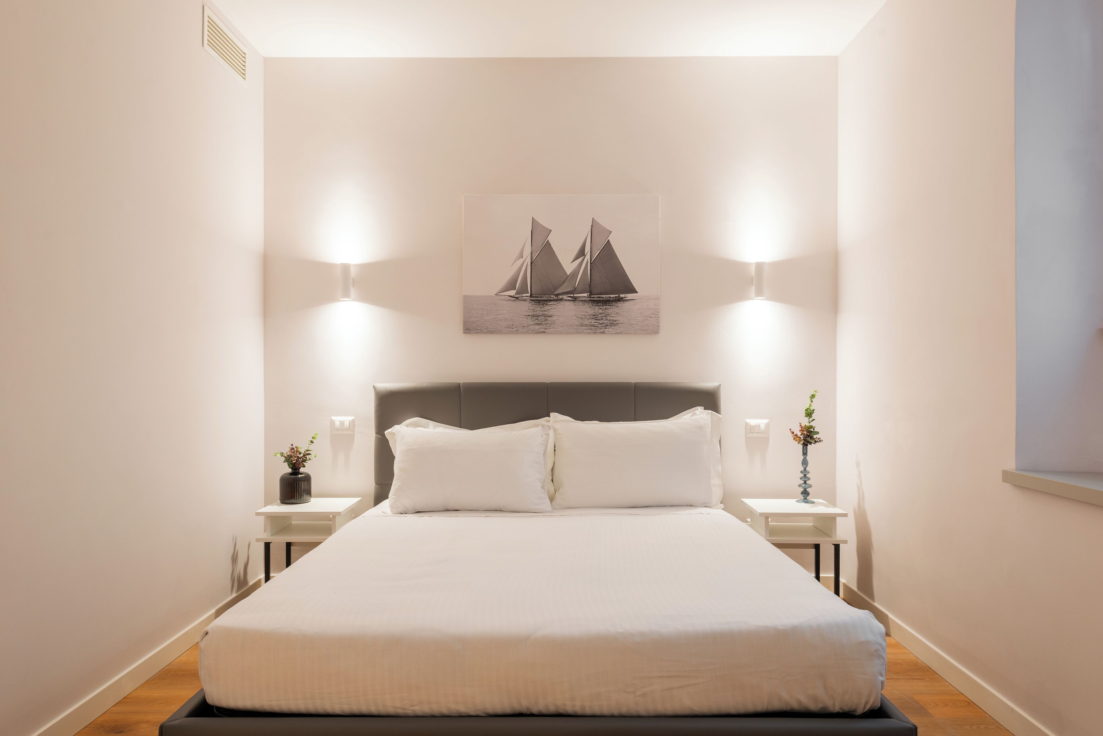 A neatly arranged bedroom with a large bed, two bedside tables, and a wall-mounted picture of sailboats.
