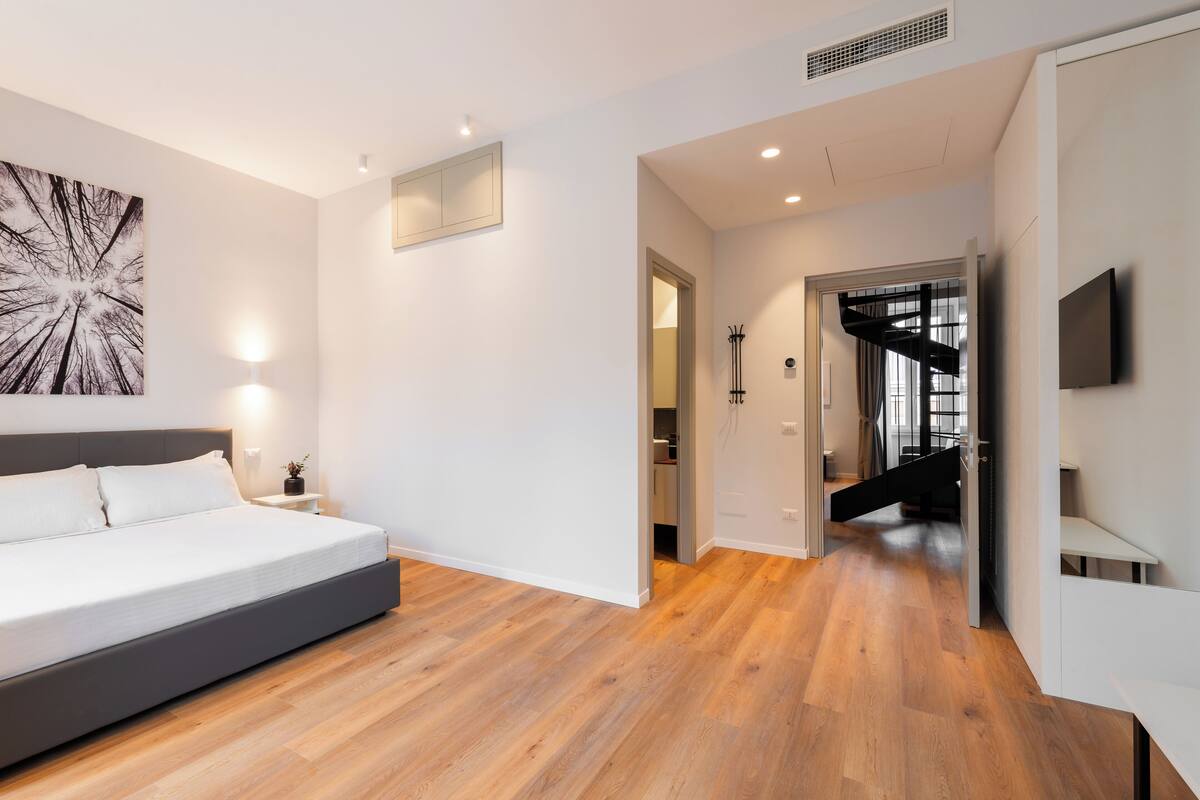Un dormitorio moderno con una cama grande, un televisor montado en la pared y una escalera que lleva a un nivel superior.