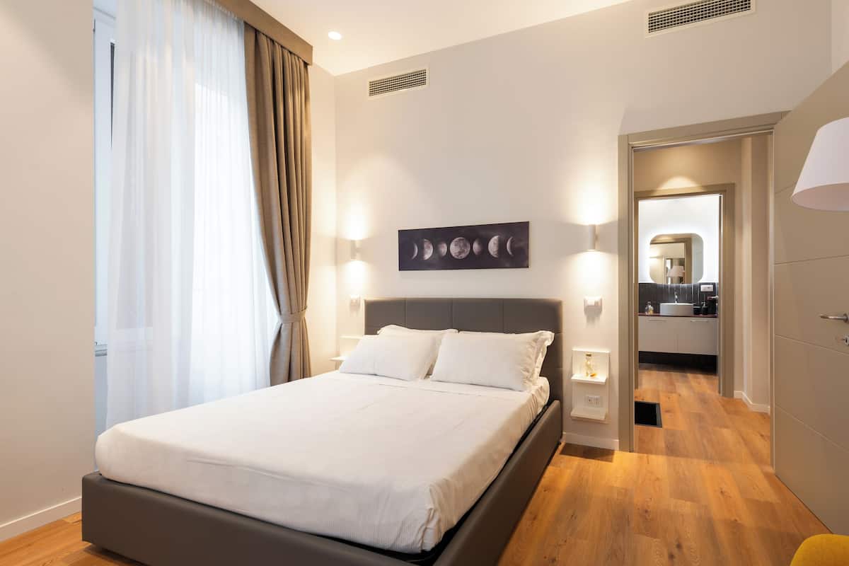 Una habitación de hotel moderna con una cama grande, un cuadro de lunas en la pared y vistas a la cocina.