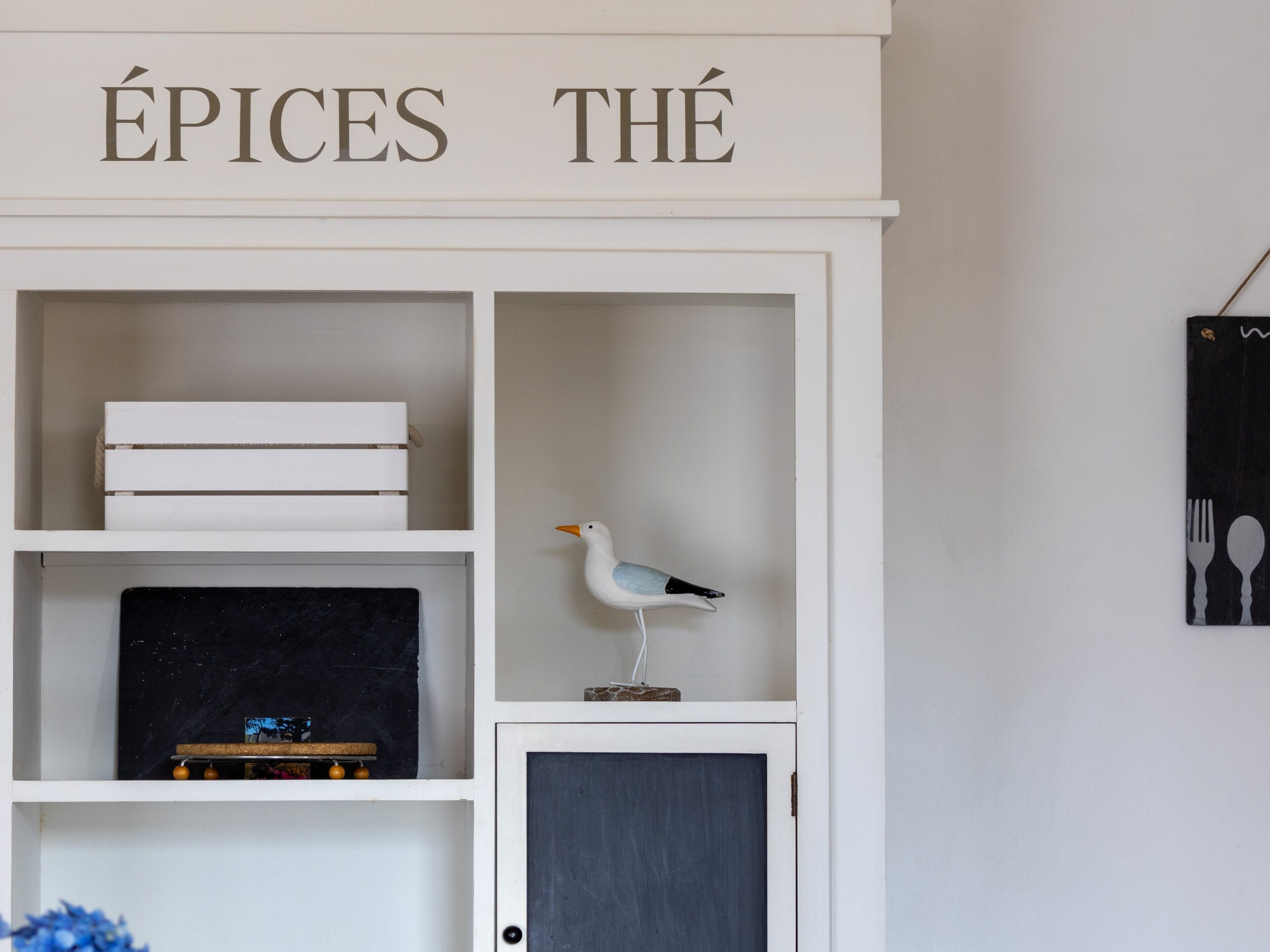 A white cabinet with shelves, a closed door, and a sign above reading 'ÉPICES THÉ'.