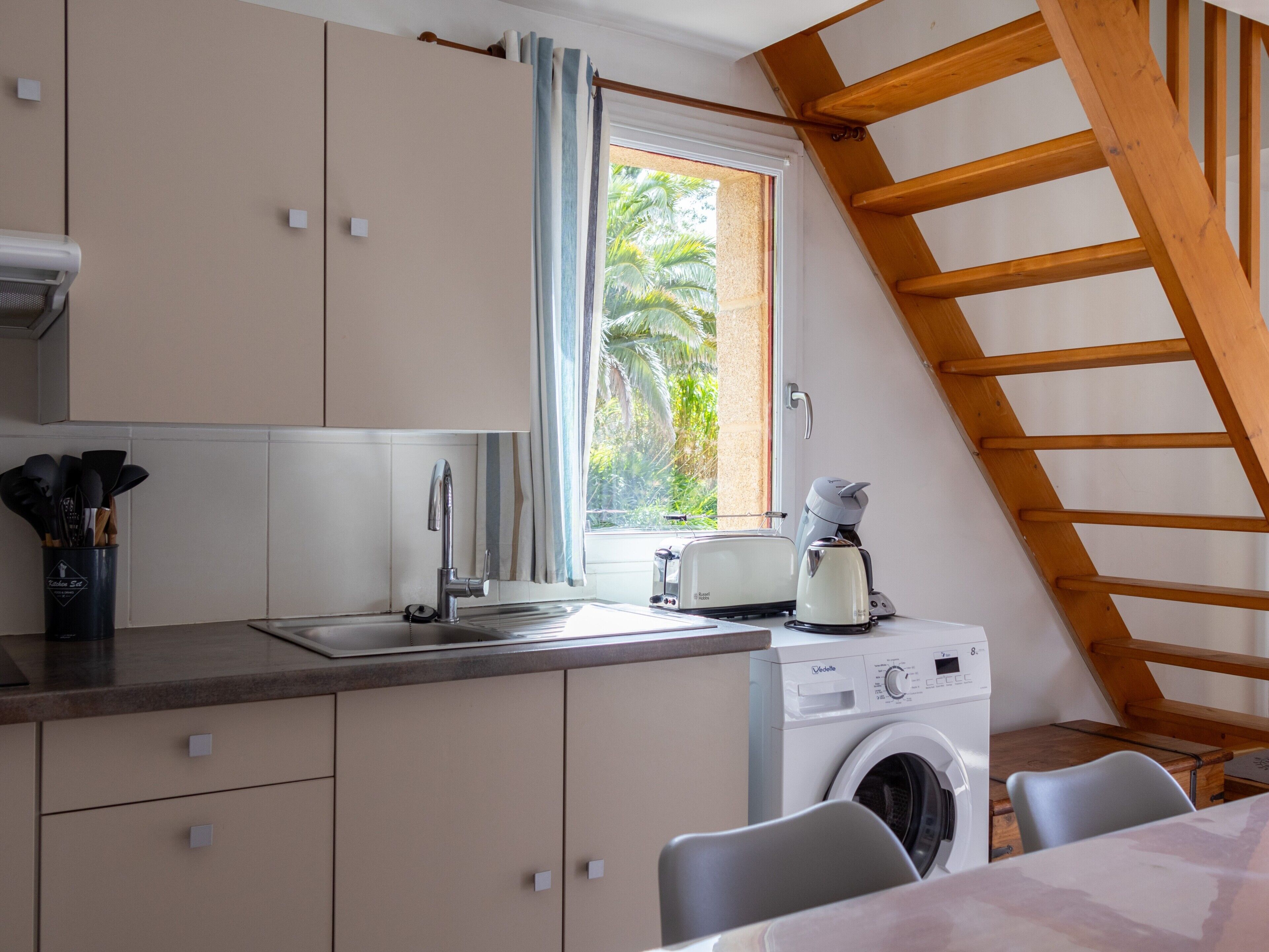 A compact kitchen with a washing machine, a toaster, and a window with curtains.