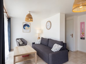 Un salon avec un canapé, une table basse, une lampe, une horloge murale et un tableau encadré.