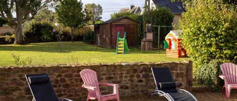 A stone wall with outdoor seating, a children's play structure, and a small shed in a garden setting.