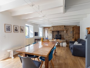 Un vaste espace de vie comprenant une grande table à manger en bois, des chaises bleues, une cheminée en pierre et un canapé bleu foncé.