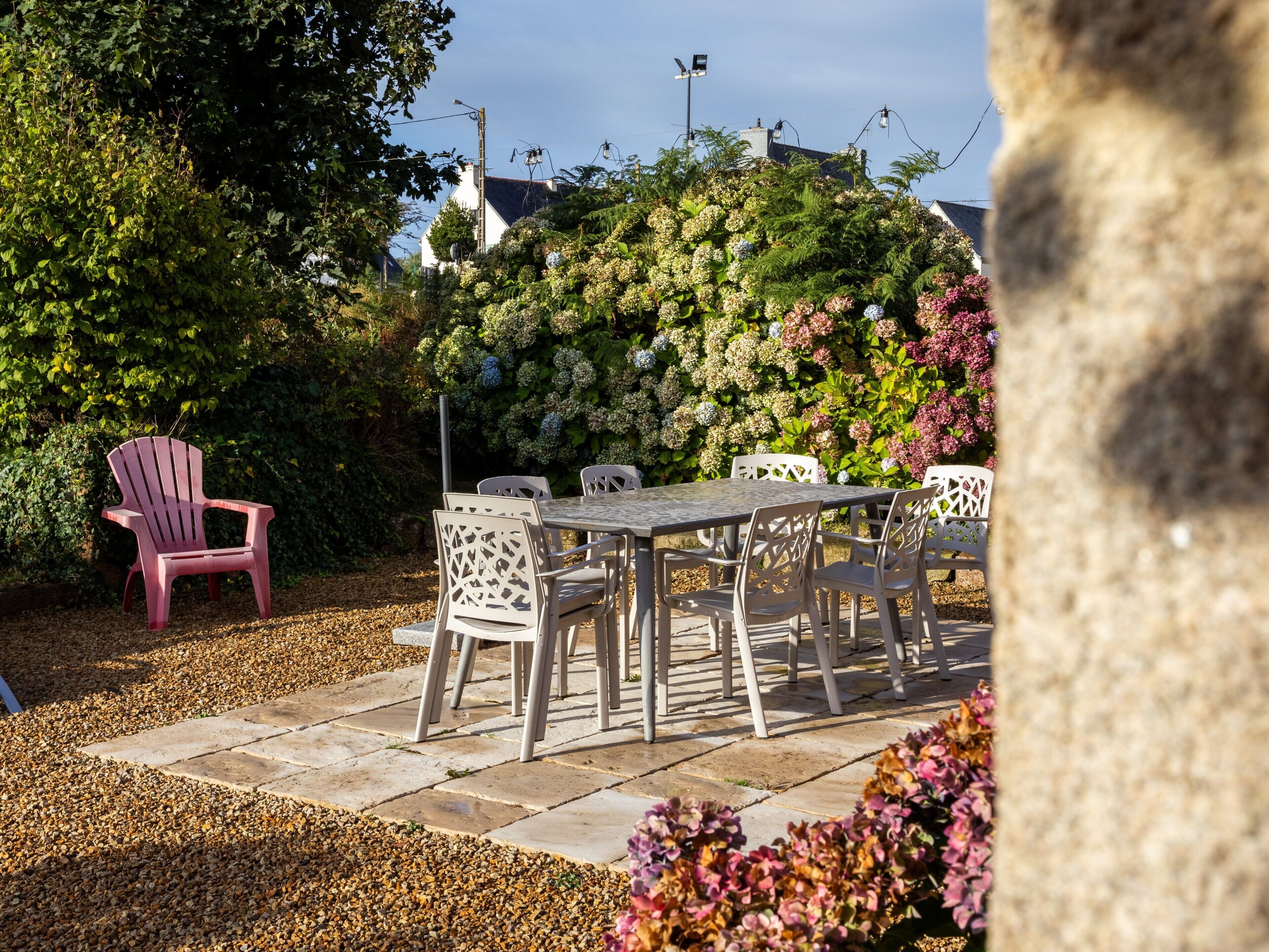 Une terrasse extérieure avec une table et des chaises, entourée d’une haie et agrémentée d’un fauteuil rose.