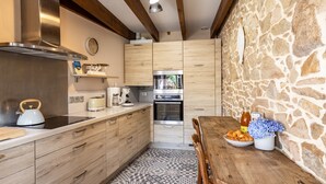 Una cocina moderna con armarios de madera, una pared de piedra y una zona de comedor con una mesa dispuesta para dos personas.