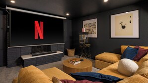 A modern living room with a large flat-screen TV displaying the Netflix logo, a fireplace, a bookshelf, and a comfortable seating area with a round coffee table. - Freshly remodeled home in Westminster. HotTub, Movie Theater, Pool Table, Arcade (Westminster)