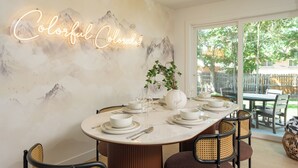 A dining area with a round table set for six, a neon sign on the wall, and a view of the outdoors through large sliding doors. - Freshly remodeled home in Westminster. HotTub, Movie Theater, Pool Table, Arcade (Westminster)