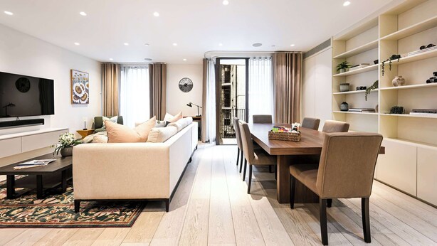 A modern living room with a sofa, coffee table, and dining area with chairs and a table. There is a TV mounted on the wall, a clock, and a bookshelf with decorative items. - Luxe 3BR/4BA Home w/ Air Con Games 5min Selfridges (Greater London)