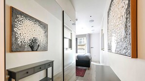 A modern hallway with a console table, a large abstract painting, and a bed in the background. - Luxe 3BR/4BA Home w/ Air Con Games 5min Selfridges (Greater London)