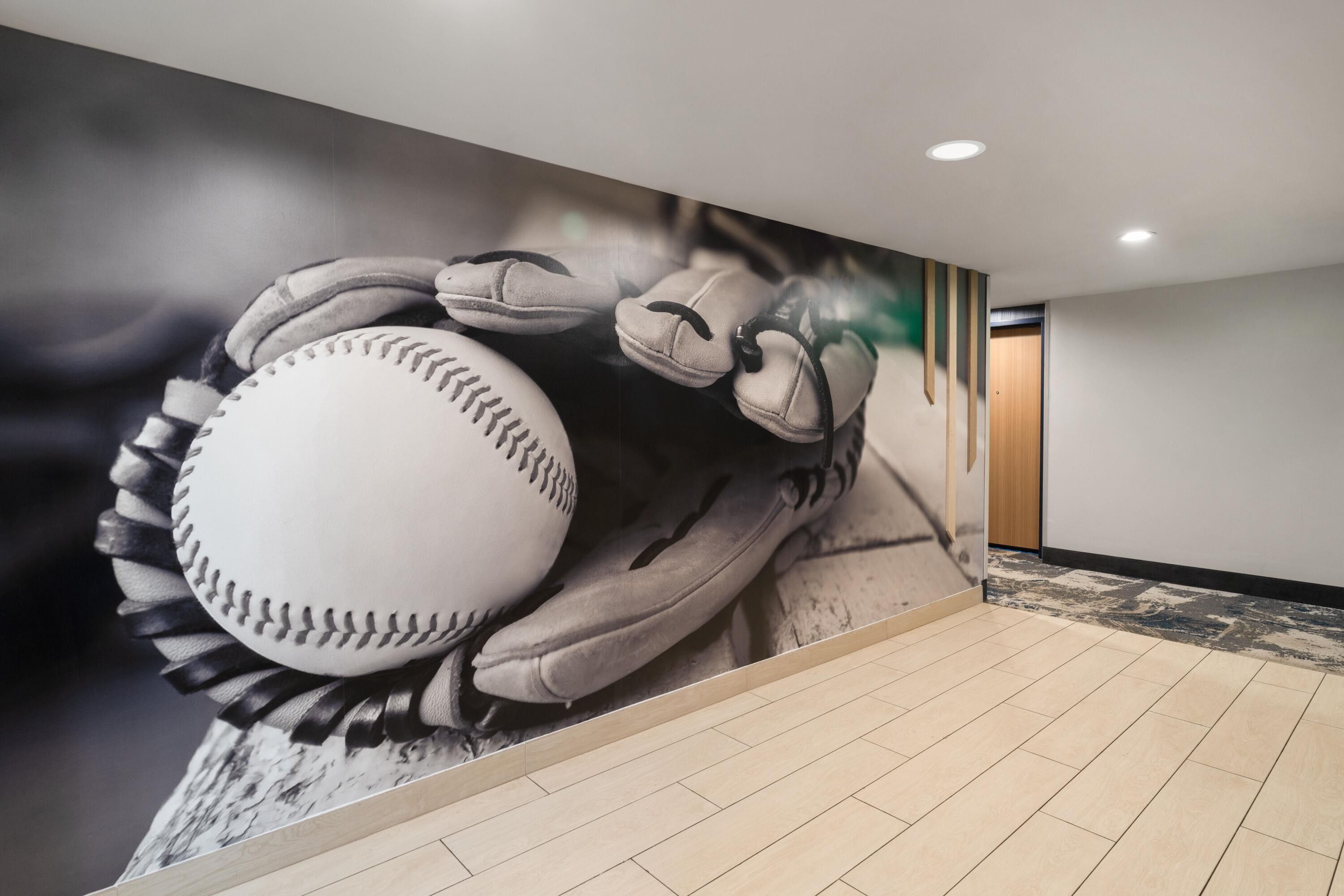 A hallway with a large mural of a baseball player holding a ball, a tiled floor, and a door in the background.