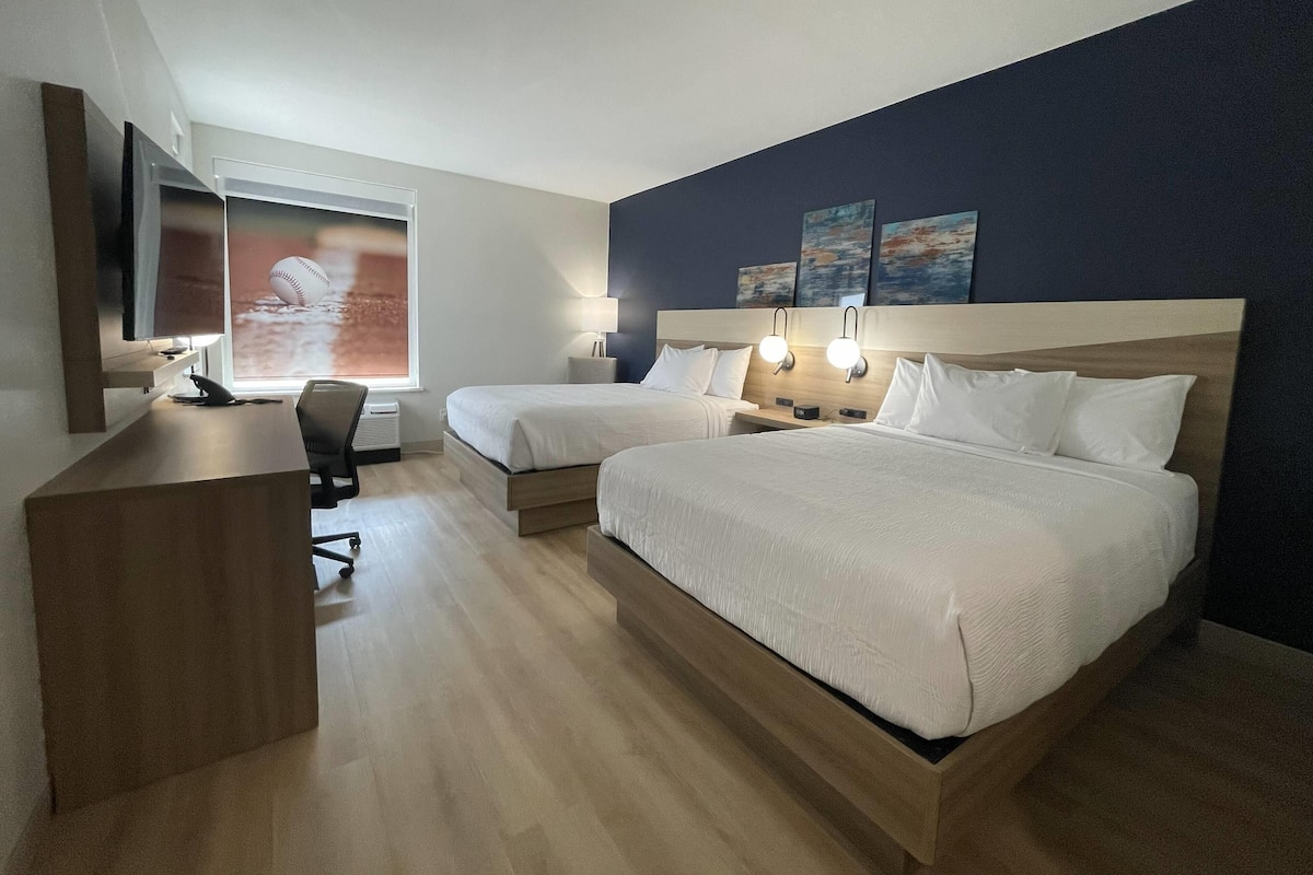 A hotel room with two beds, a desk, a chair, and a TV.