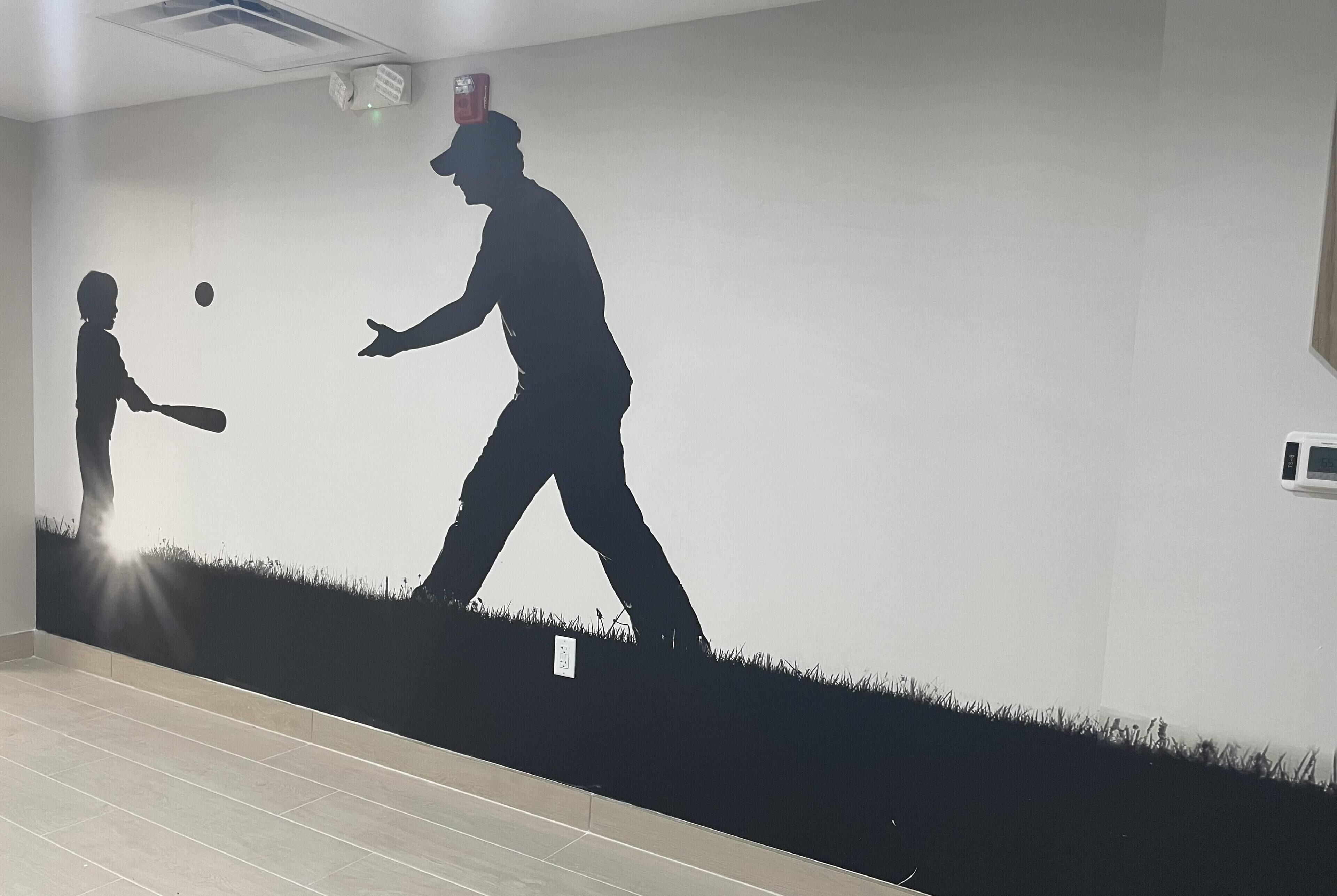 A room with a wall mural depicting a silhouette of a person playing baseball with a child.
