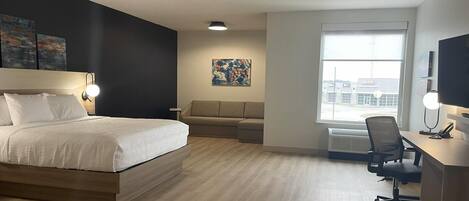 A modern hotel room with a large bed, a desk with a chair, a sofa, and artwork on the walls.