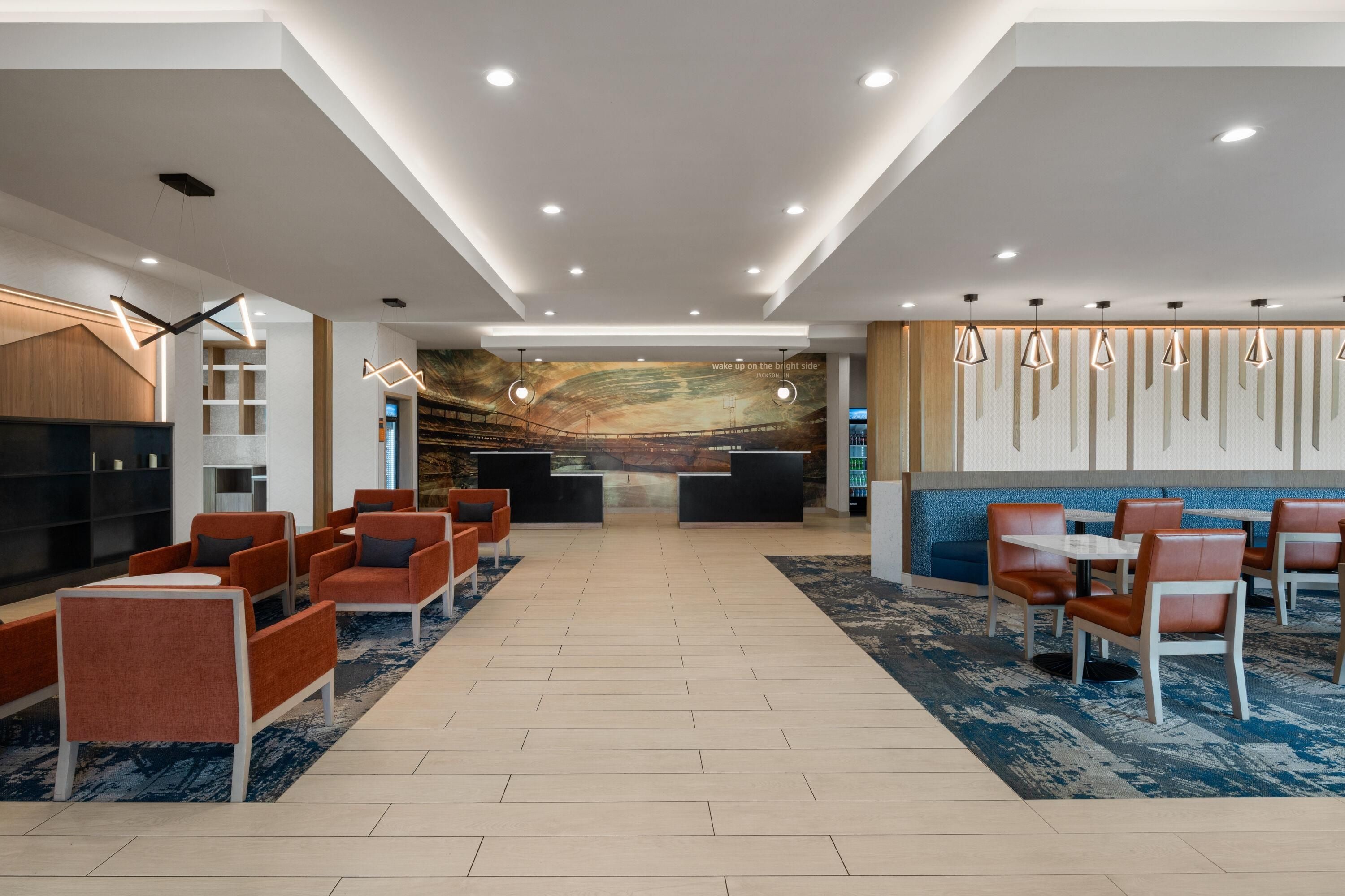 A modern hotel lobby with a reception desk, seating area, and a large mural.
