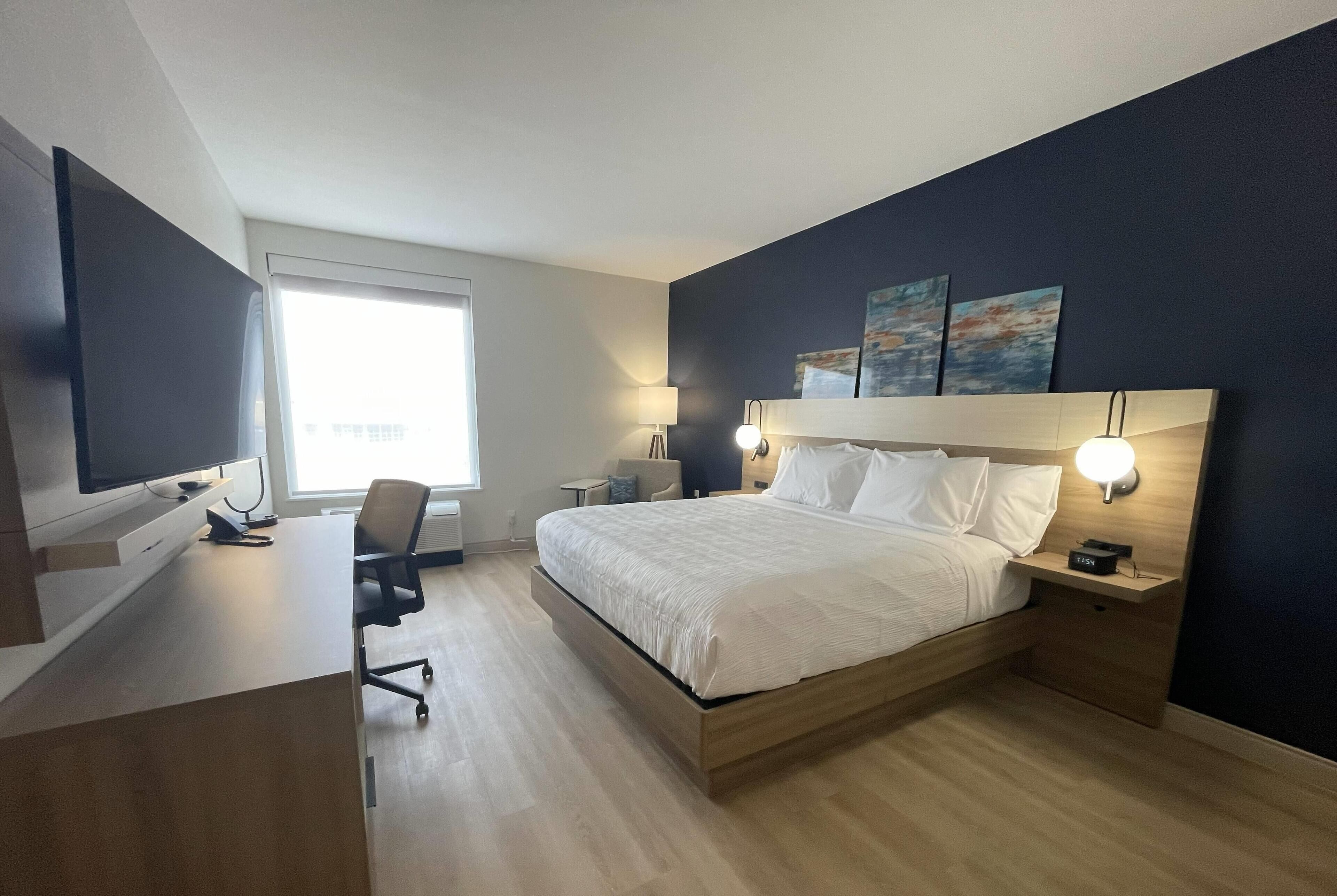 Ett modernt hotellrum med en stor säng, ett skrivbord och en tv.