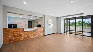 A reception area with a wooden reception desk, a large mirror, and a bench. - Echo Suites Extended Stay By Wyndham Naples (Naples)