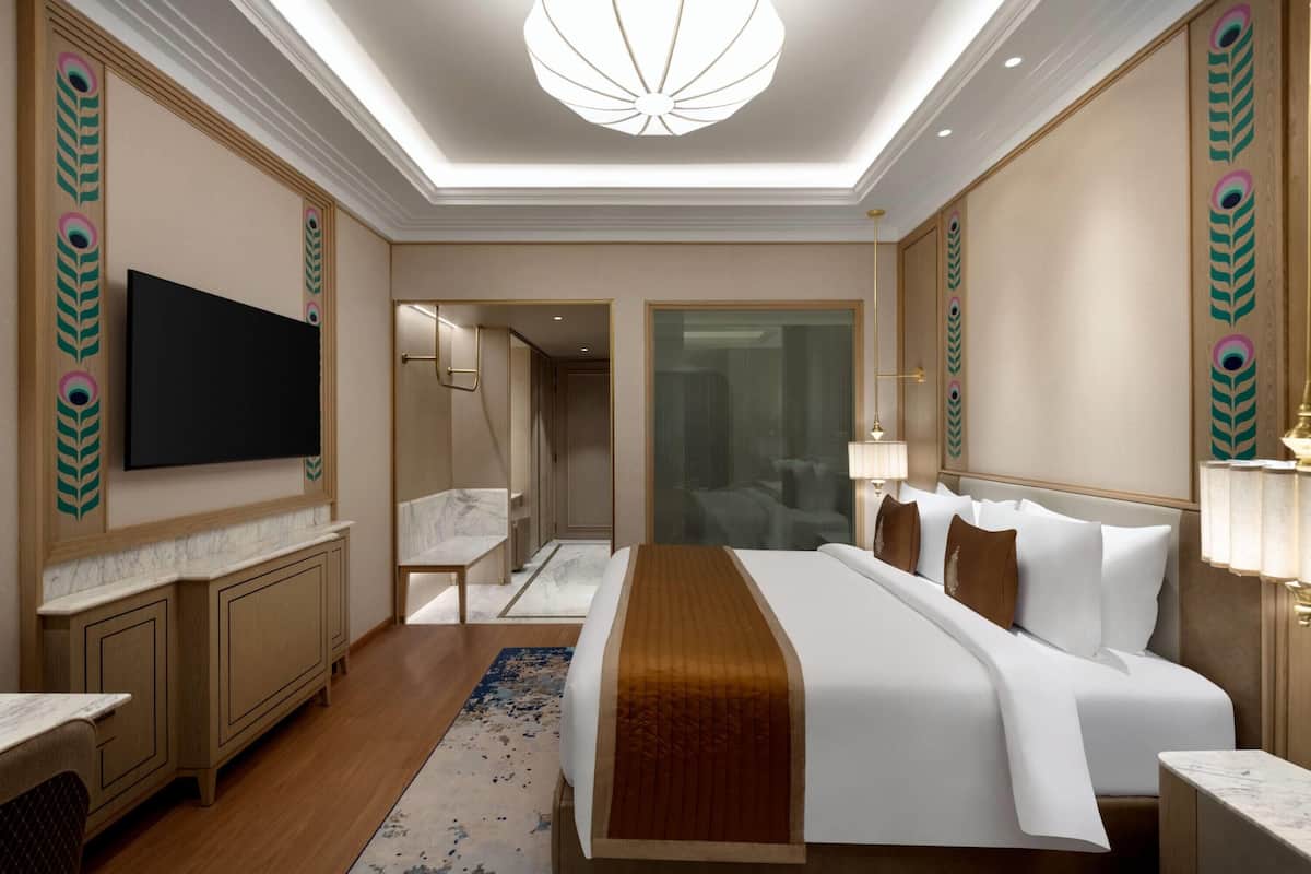 Ein modernes Hotelzimmer mit einem großen Bett, einem Flachbildfernseher, einem Badezimmer mit Duschkabine und einem Flur zu einem weiteren Zimmer.