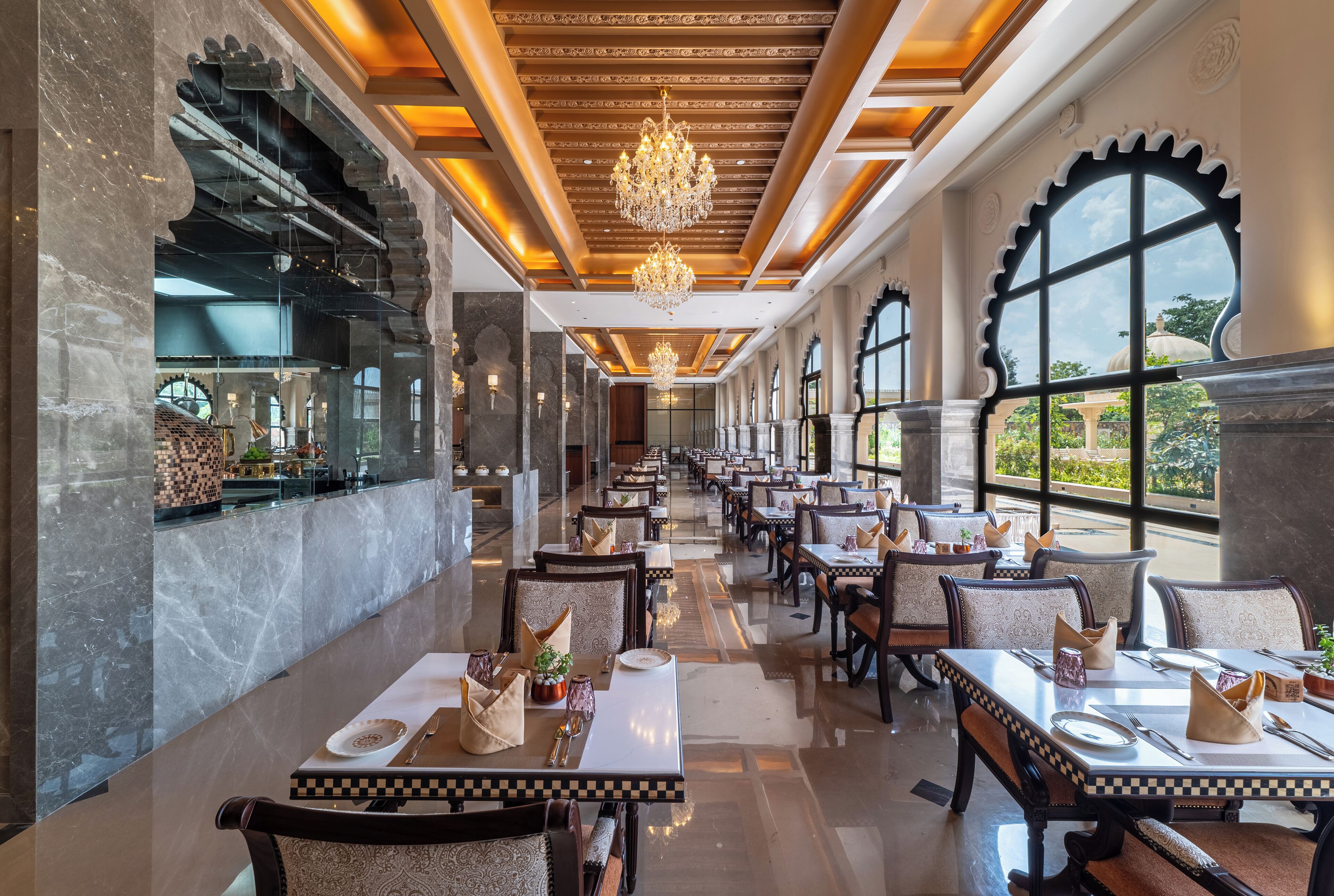 Un restaurante espacioso con paredes de mármol, candelabros y vistas a zonas verdes.