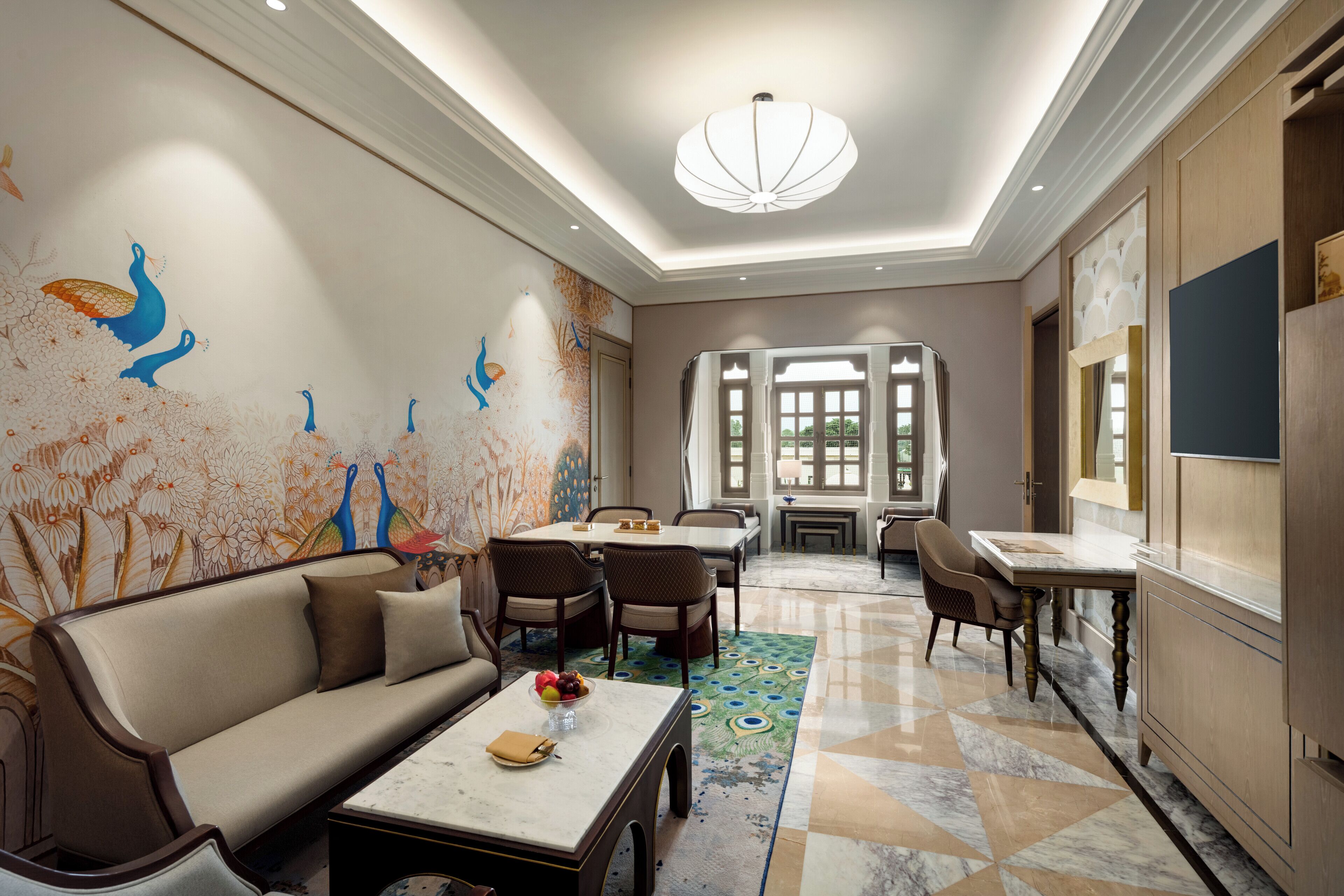 A spacious room with a sofa, dining table, chairs, and a decorative peacock mural on the wall.