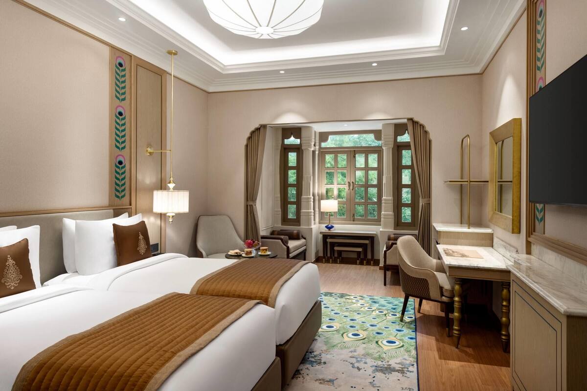 Ein Hotelzimmer mit einem großen Bett, einem Schreibtisch, einem Stuhl, einem Fernseher und einem Vorhangfenster.