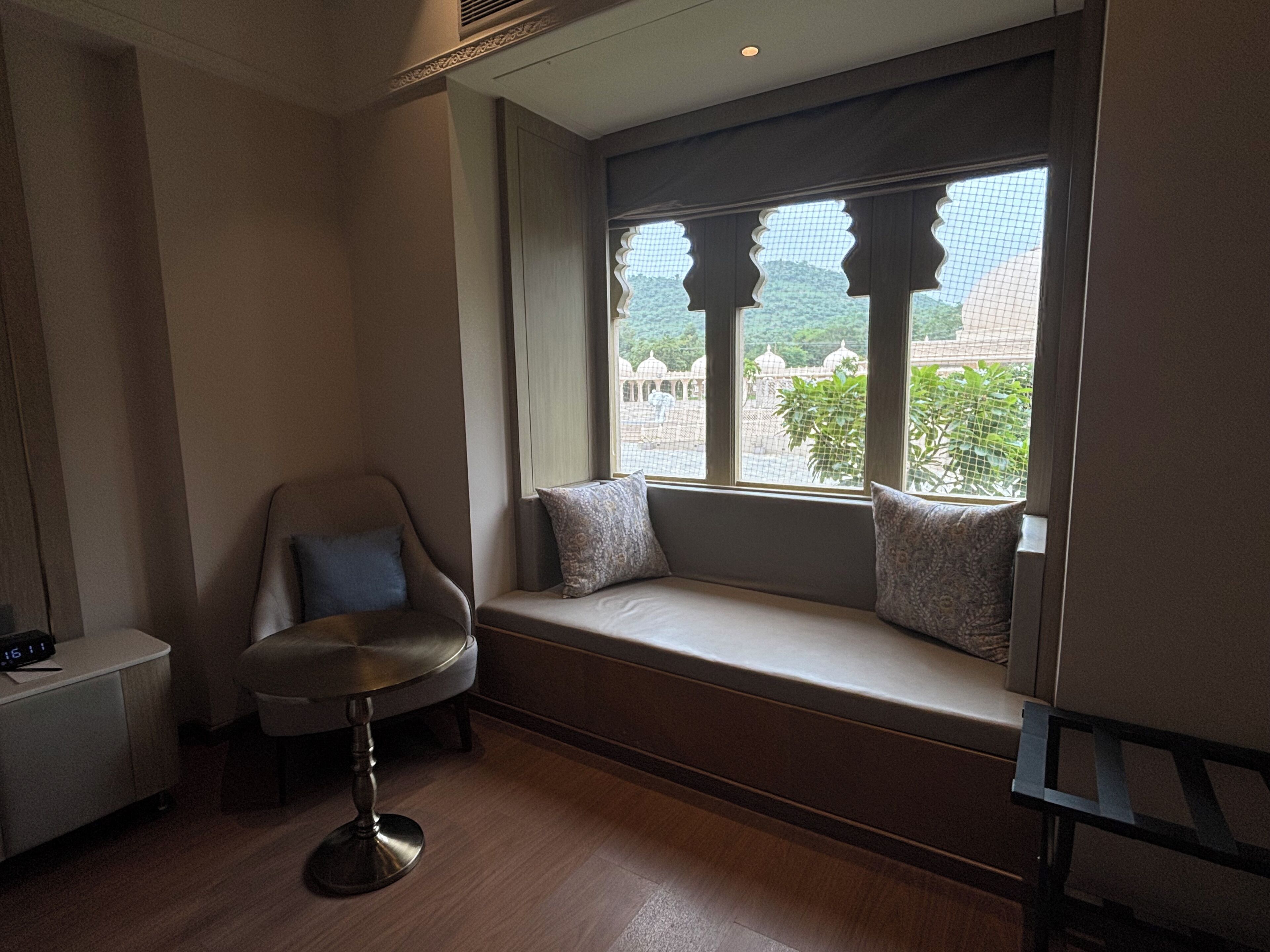 A room with a built-in bench by a window, a chair, and a small table with a clock.