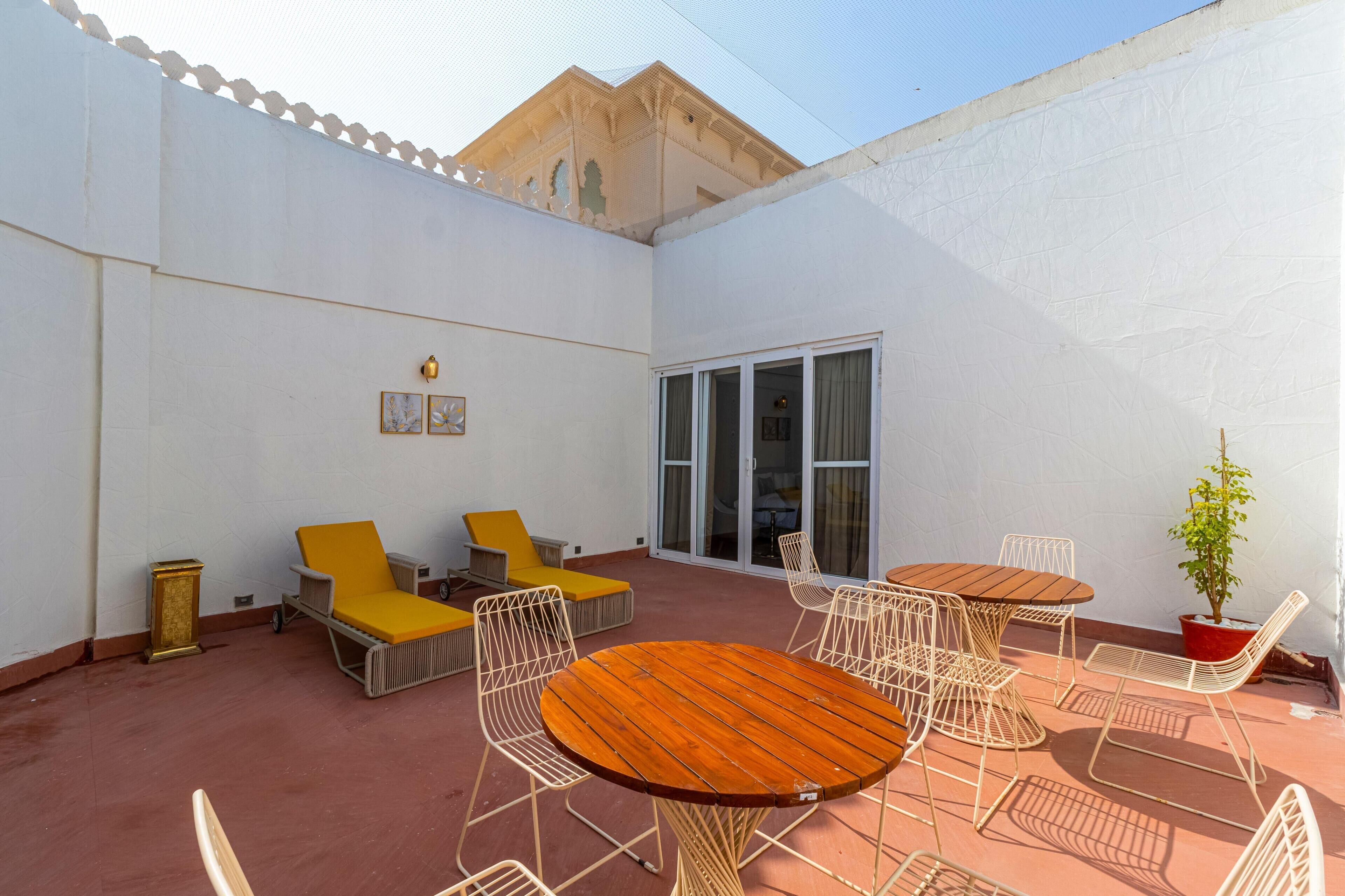 Un patio con una mesa y sillas de madera redondas, un sofá amarillo y una planta en maceta.