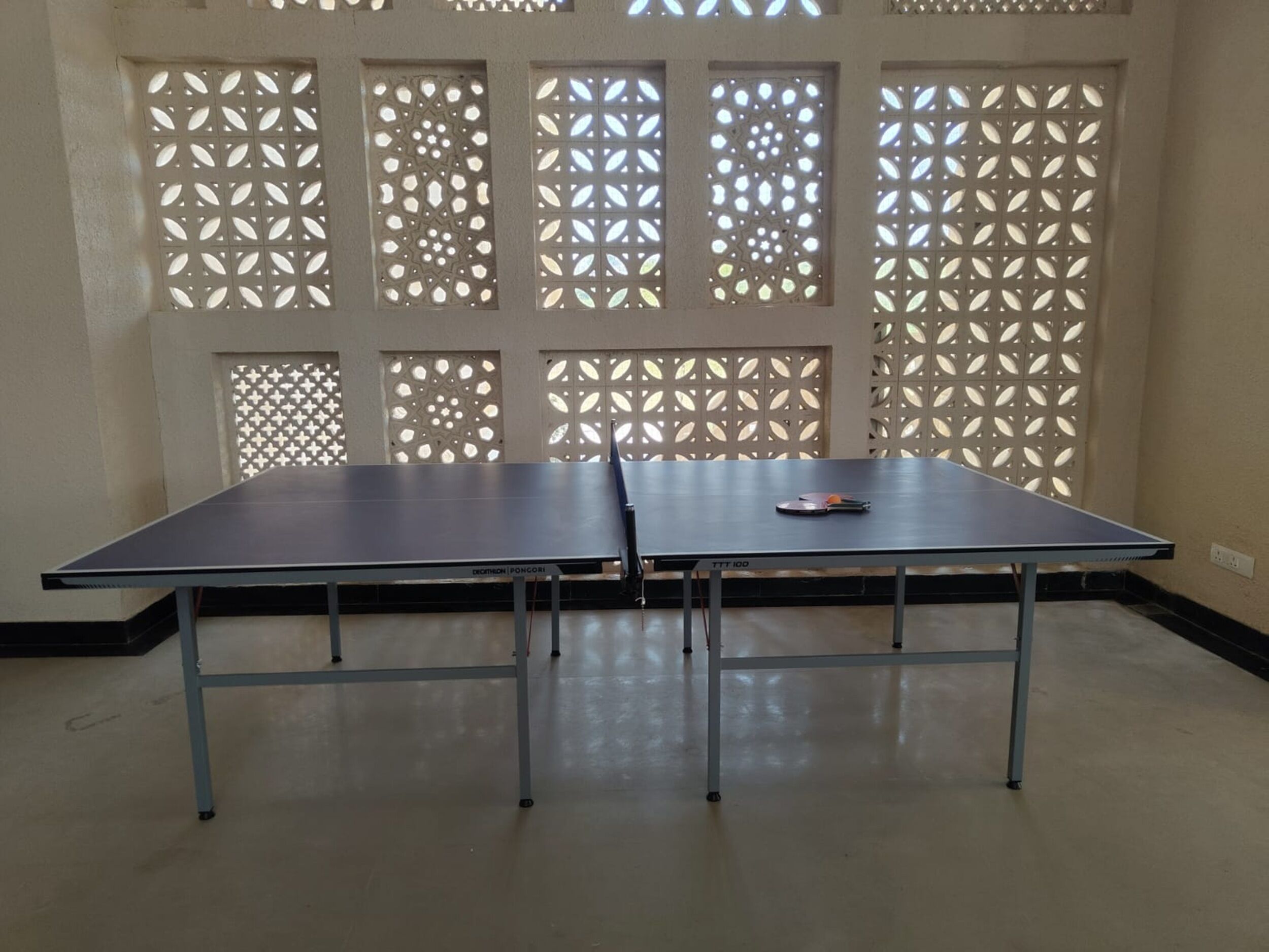 Une table de ping-pong dans une pièce dont les fenêtres sont ornées de motifs.