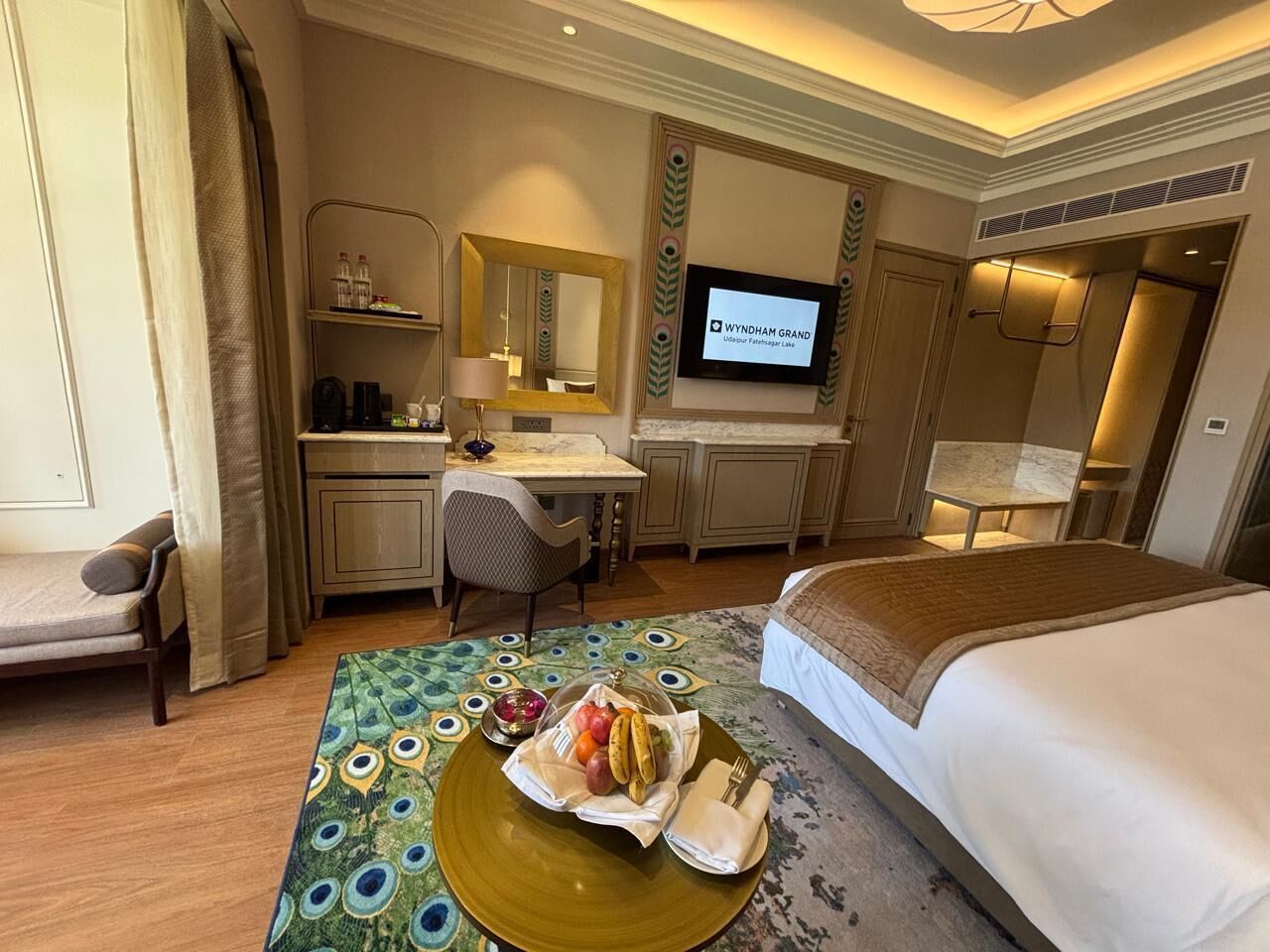 A hotel room with a bed, desk, chair, and a television displaying 'WYNDHAM GRAND'.