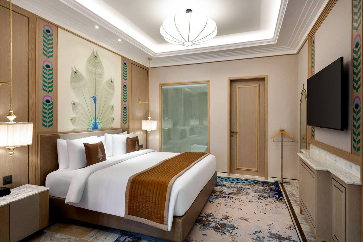 Ein Hotelzimmer mit einem großen Bett, einem Fernseher, einem Spiegel und einer Wanddekoration mit Pfau-Motiv.